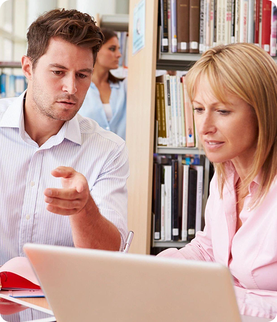 A man and woman sitting at a table looking at a laptop.