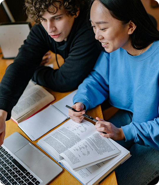 Two people are studying at a table with papers.