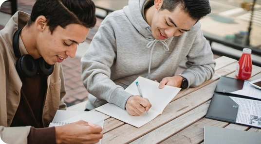 Two young men sitting at a table writing on paper.