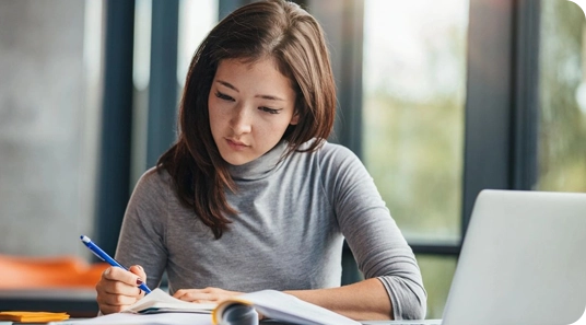 A woman sitting at a table writing on paper.