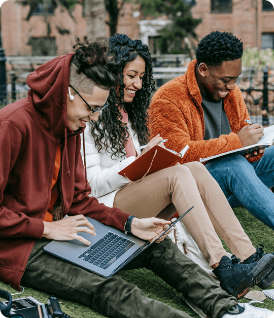 Three people sitting on the grass with laptops