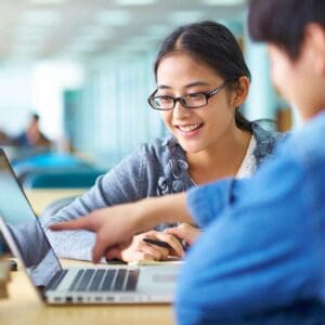 Two people sitting at a table with laptops.