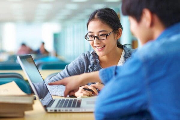 Two people sitting at a table with laptops.