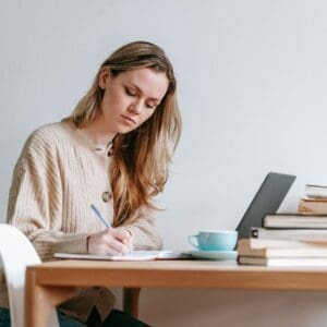 A woman sitting at a table writing on paper.
