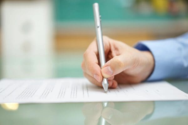 A person writing on top of paper with a pen.